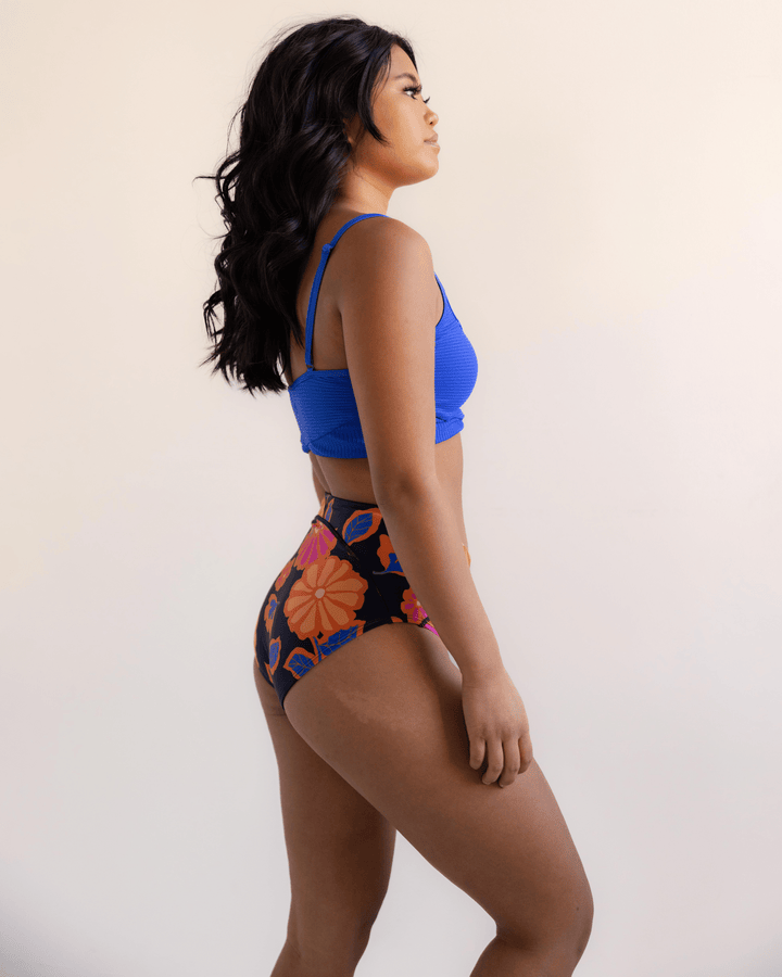 Side View studio picture of a girl in a blue bikini top and a floral swimsuit bottom