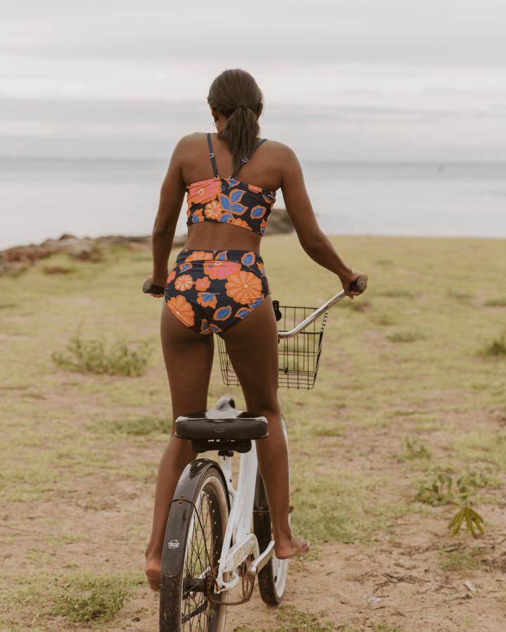 Girl standing up riding her bike to the beach in a floral bikini set.